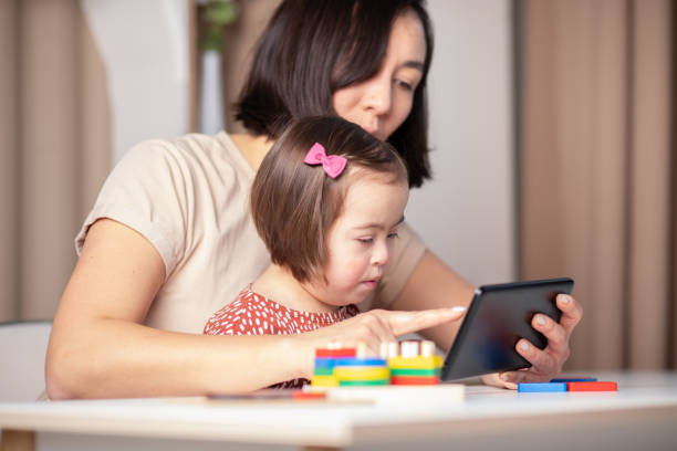 istock mother and child with down syndrome are talking on video call using mobile tablet, study online with teacher 1367510341