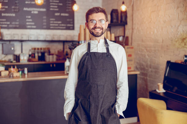 istock Cheerful male worker in apron standing in cafe 1367511048
