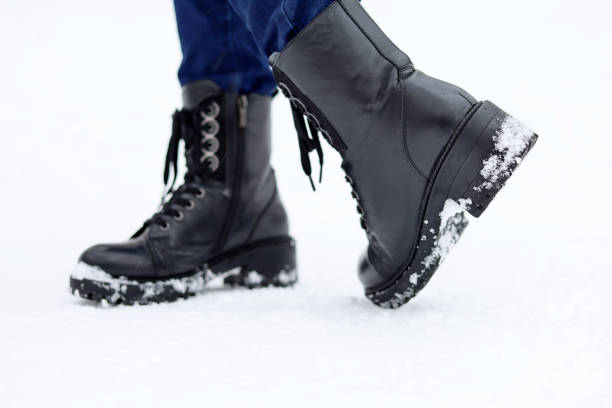 istock Female legs in black leather lace-up boots on a snow 1367520278