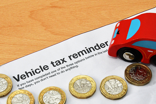 Top of a vehicle tax reminder letter with one pound coins anda model car. No people. Cost of running a car concept.