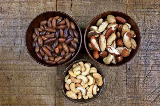 Three types of Brazilian chestnuts, in bowls of varying sizes, on rustic wooden table
