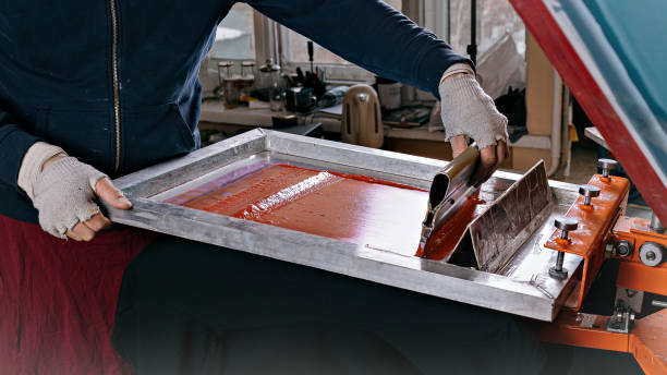 istock silk screen textile printery. serigraph printing production. male hand with a squeegee. creating print on t-shirt in workshop 1367527401