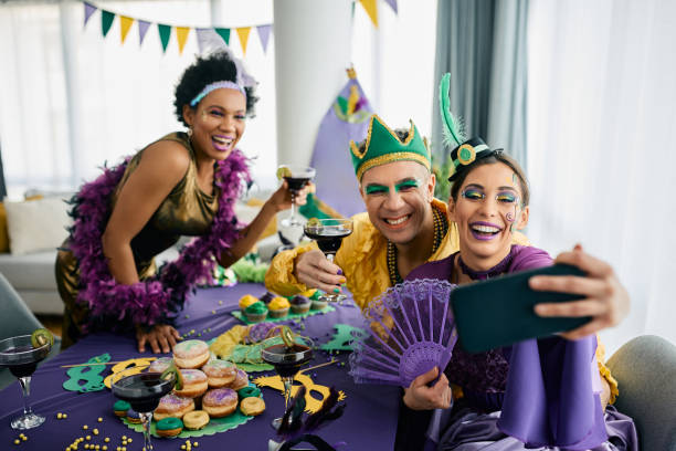amici multirazziali che indossano costumi di carnevale e si fanno selfie mentre celebrano il mardi gras a casa. - carnival mask women party foto e immagini stock