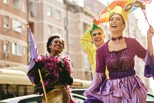 Multi-ethnic friends having fun and laughing while wearing costumes and participating in Mardi Gras parade.