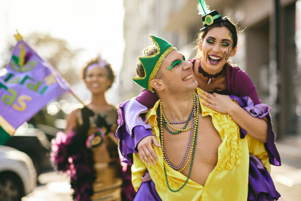 cheerful couple piggybacking and having fun on mardi gras street parade. - carnival parade imagens e fotografias de stock
