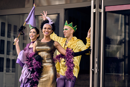 Happy African American woman and her friends wearing costumes and having fun while going on Mardi Gras street parade.