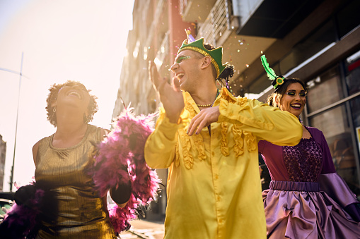 Group of happy people in carnival costumes dancing and having fun during Mardi Gras festival on the street.