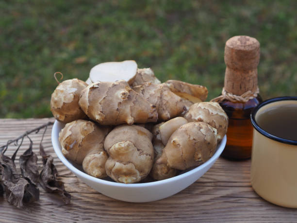 Fruits of the Jerusalem artichoke plant, syrup and natural juice in mug on wooden table. Healthy helianthus tuberosus root vegetables and drinks for vegan, vegetarian nutrition and diabetes prevention and treatment frutos de la planta de alcachofa de jerusalén, jarabe y jugo natural en taza sobre mesa de madera. vegetales y bebidas saludables de raíz de helianthus tuberosus para la nutrición vegana, vegetariana y la prevención y el tratamiento de la diabetes