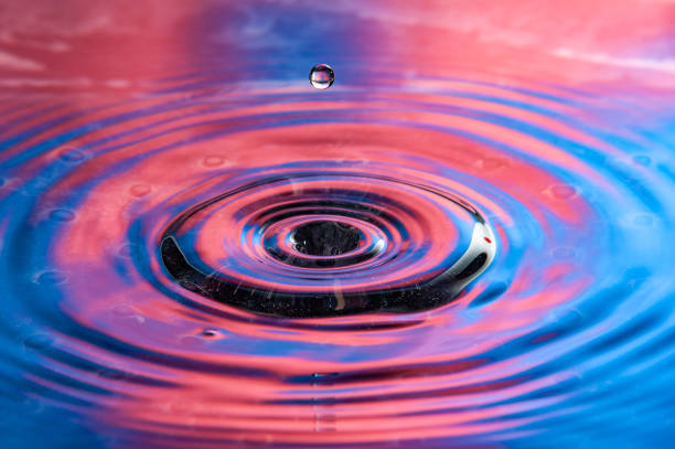 istock Single water drop falling towards a vibrant red and blue water splash. High speed water drop photography. 1367532578