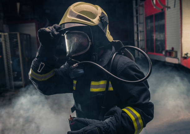 retrato de um bombeiro usando bombeiros usando máscara de oxigênio. fundo escuro com fumaça e luz azul. - turnouts - fotografias e filmes do acervo