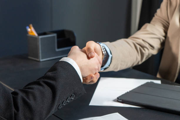 istock Businessmen shaking hands in the office with computer 1367537333