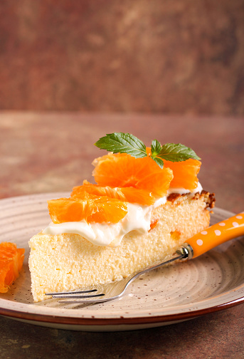 Slice of citrus cheesecake with cream and clementine on top
