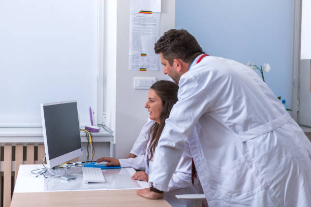 Two nurses ( female physicians ) and a male doctor standing next to a pc, mac ( desktop computer ) in the doctor's office while discussing a medical report.