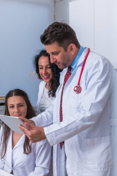 istock Two nurses ( female physicians ) and a male doctor looking in a tablet at the doctor's office while discussing a medical report ( patient's health problems ). 1367542630