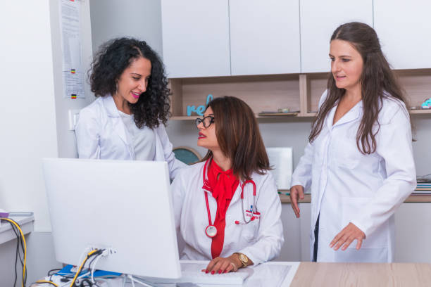 istock ( Medical Team ) Female doctor ( medic ) in her 30's working on her computer while two female nurses stand next to her and discuss a patients illness. 1367542633