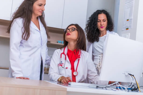 istock ( Medical Team ) Female doctor ( medic ) in her 30's working on her computer while two female nurses stand next to her and discuss a patients illness. 1367542641