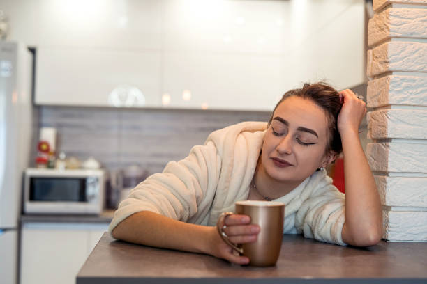 giovane ragazza con bei capelli in camice bianco che beve caffè in cucina al mattino. - yawning women drink coffee cup foto e immagini stock