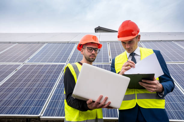 gutaussehende junge männer in schutzhelmen mit dokumenten stehen in der nähe der neu installierten paneele. - green business stock-fotos und bilder