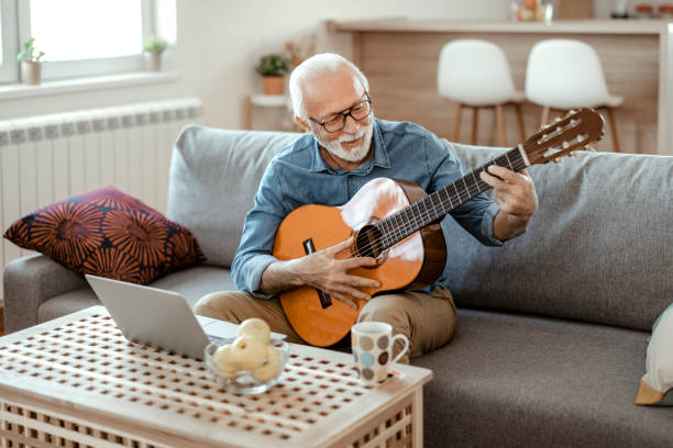 istock Bearded Senior Man Playing Guitar and Watching Online Lessons 1367548705