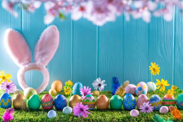 istock Easter eggs on turf grass and blue wooden wall with spring flowers 1367548958