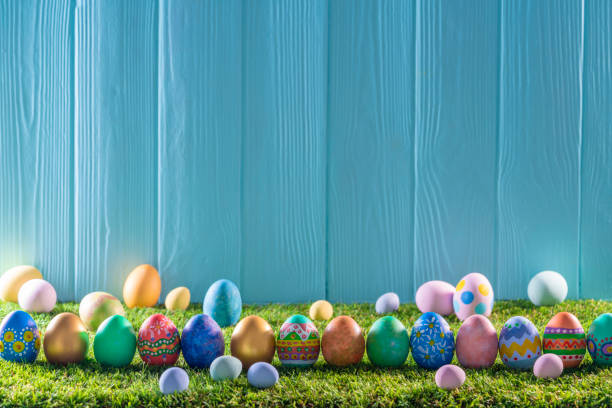 istock Easter eggs on turf grass and blue wooden wall with spring flowers 1367548989