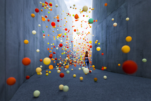 Woman walking in abstract concrete corridor with large amount of exploding spheres. 3D generated image.