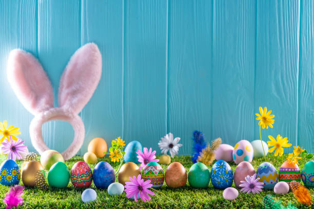 istock Easter eggs on turf grass and blue wooden wall with spring flowers 1367549986