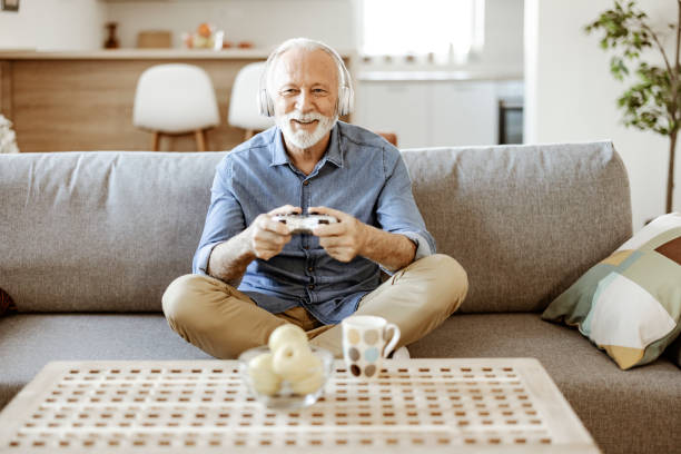 istock Bearded Senior Man in Headphones Playing Console 1367550026