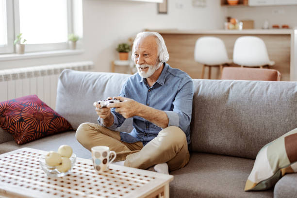 istock Bearded Senior Man in Headphones Playing Console 1367550029