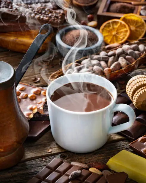 Melted hot chocolate cup with vintage copper chocolate pot and cocoa beans with assorted bars on rustic wood