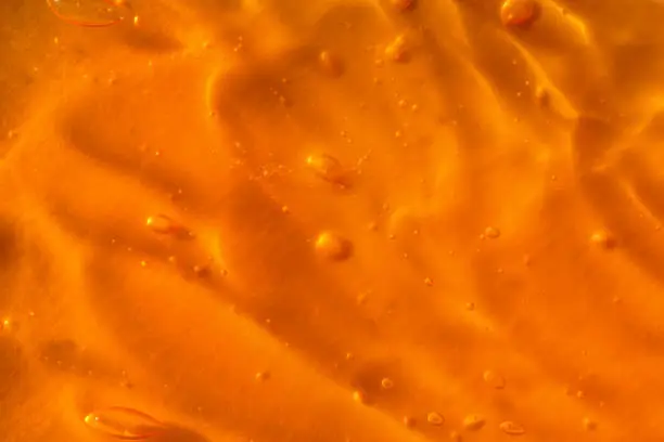 Photo of Texture of transparent yellow gel with air bubbles and waves on orange background