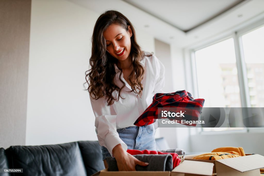 Woman sorting clothing and packing donation box Decluttering Stock Photo