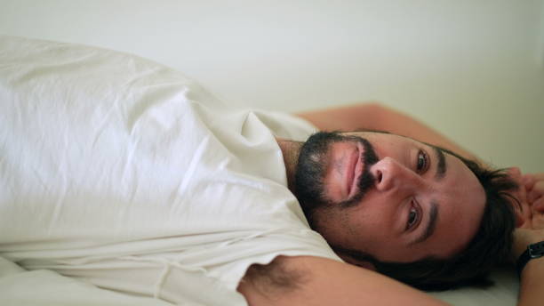 istock Young man lying in bed looking at camera smiling 1367553315