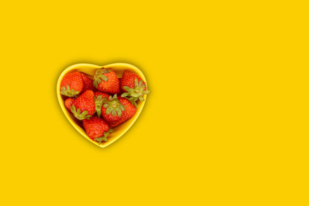 Fresh strawberries on a red heart-shaped plate on a wooden rustic table. A delicious Valentine's dessert