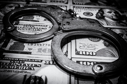 A pair of worn handcuffs with hundred dollar bills as a concept for bail, criminal justice reform, police budgets, the costs of crime or many others