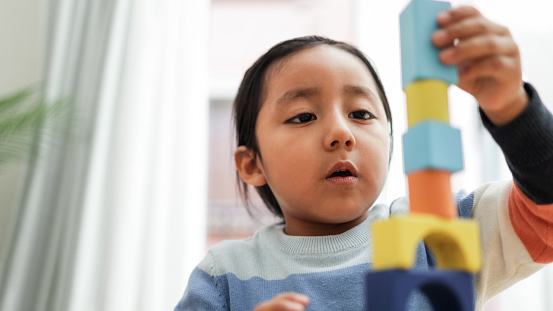 Niño asiático jugando con bloques de colores en casa - Juegos educativos de jardín de infantes - Concéntrese en la boca del niño photo