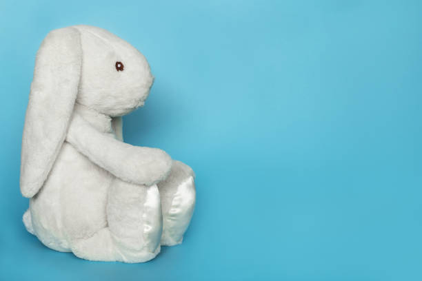 Stuffed bunny on blue background. Easter concept. Cute white toy soft bunny sitting on colored background. Copy space for text