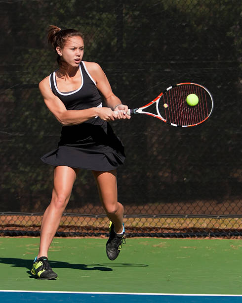 Female high school tennis player hits backhand Very fit girl teenage tennis player smacks backhand, ball is frozen on racket head. backhand stroke stock pictures, royalty-free photos & images
