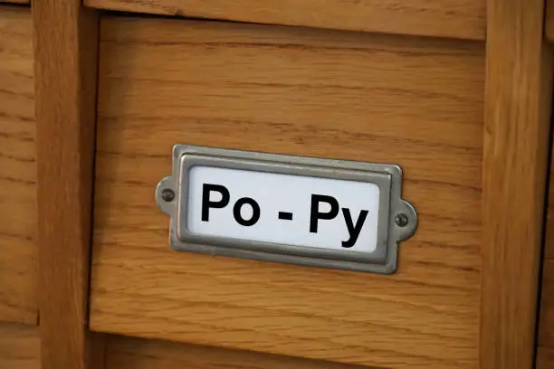 Photo of The syllables Po and Py are printed in black on the drawer of an old wooden library catalog
