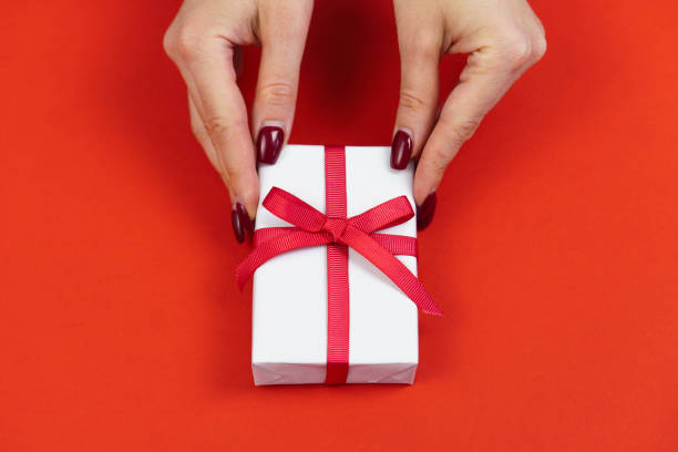 istock Woman hands hold white gift box with red bow on red table. Valentines day or bithday present concept 1367567334