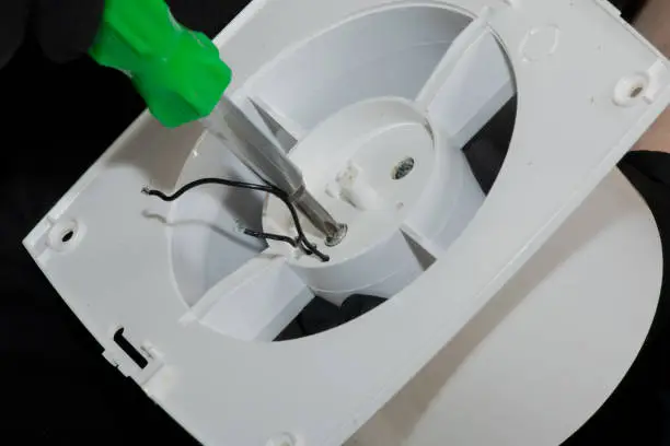 Photo of The process of assembling the kitchen exhaust fan after cleaning the wash. A man works with a screwdriver in his hands