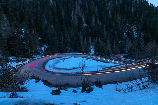 Light trails on a winding mountain pass road with hairpin bends in the European Alps at dusk in winter