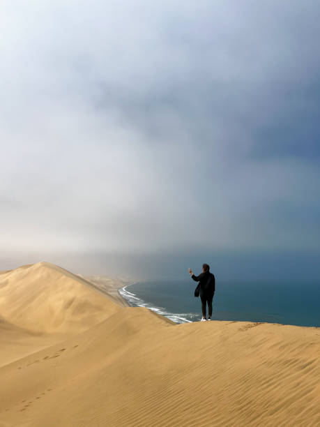 istock A young woman stands sandy dunes on seashore. Sandwich Harbour in Namibia 1367575308