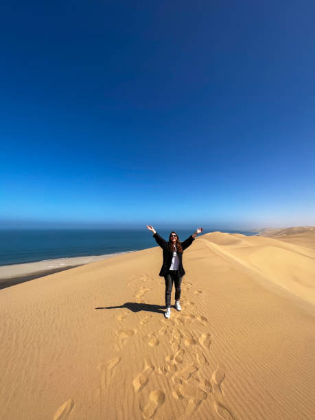 istock A young woman walks along sandy dunes on seashore. Sandwich Harbour in Namibia 1367575413