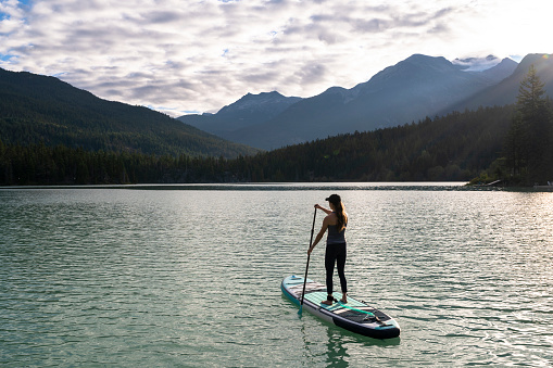 Woman stand up paddle boarding on a pristine mountain lake. Summer vacations in British Columbia.