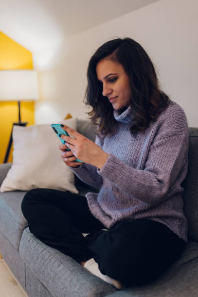 istock Hispanic woman using smartphone while sitting on the couch at home 1367581594