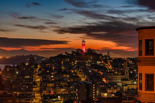 An aerial view of Coit Tower and the San Francisco Bay in the distance with a dramatic and vibrant sky.