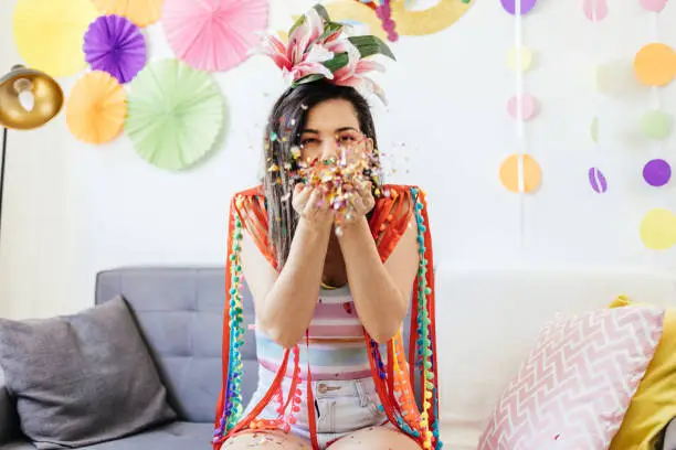 Brazilian Carnival. Young woman enjoying the carnival at home blowing confetti