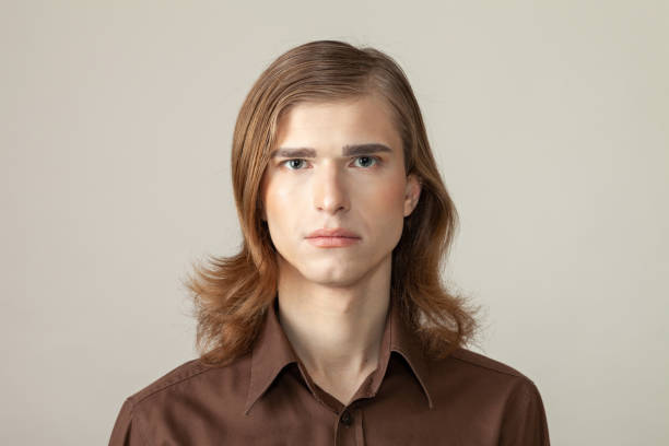 Close-up studio portrait of a non-binary person Close-up studio portrait of a non-binary person with long brown hair with make-up in a brown shirt on a beige background non binary gender photos stock pictures, royalty-free photos & images