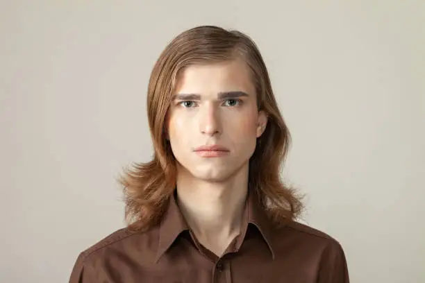 Close-up studio portrait of a non-binary person with long brown hair with make-up in a brown shirt on a beige background